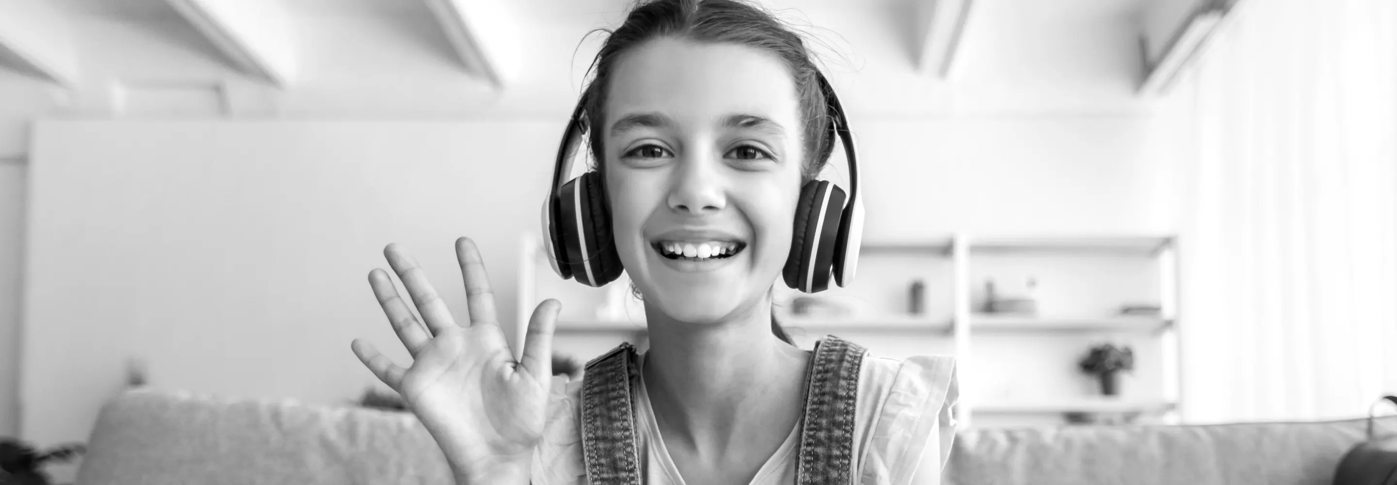 A student wearing headphones smiles and waves during an online lesson