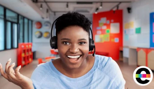 A smiling student wearing a headset talks with an educator over video.