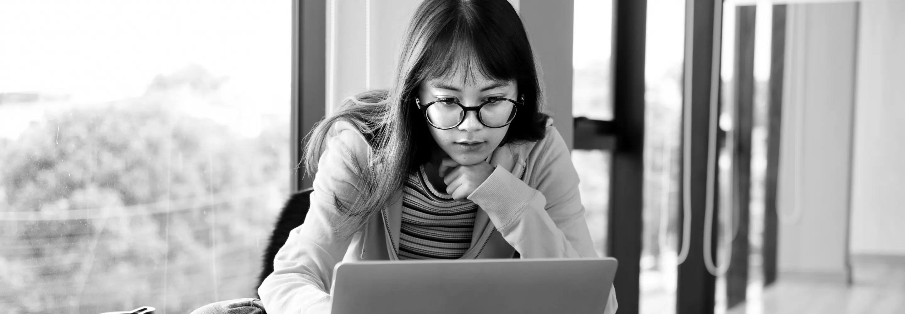 A student in glasses studies a laptop screen