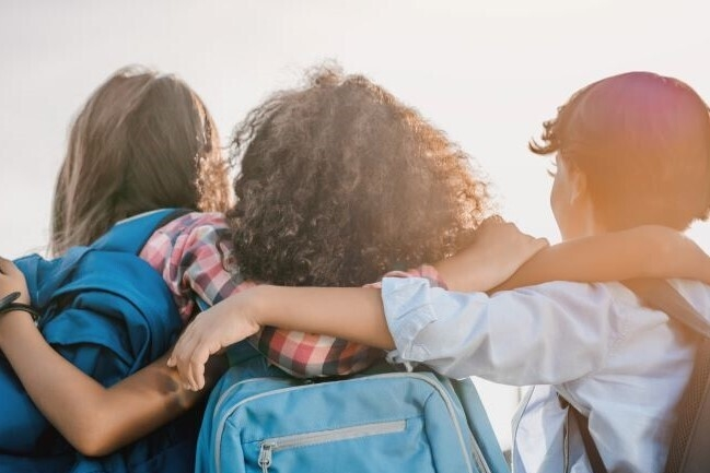 Three students with backpacks facing the sun